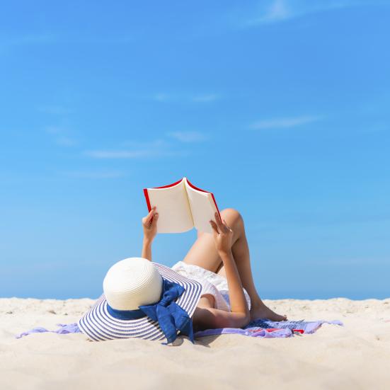 Kvinde ligger på en eksotisk strand og læser