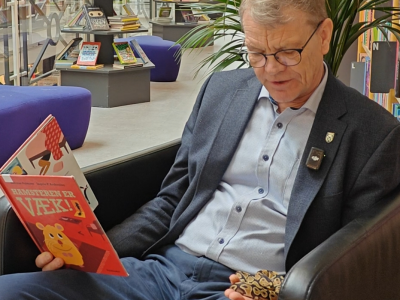 Borgmester Mikael Klitgaard sidder i lænestol på biblioteket og læser højt for pythonslange, som han holder i hånden.