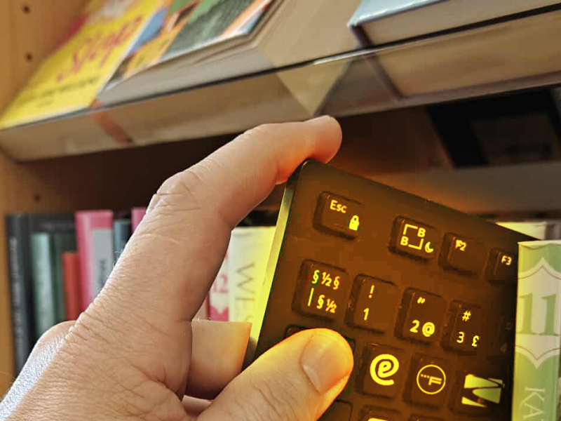 Nærbillede af hånd, der trækker et computertastatur ud mellem bøgerne på en hylde. Flere af tastaturets knapper er udskiftet med logoer for eReolen, Filmstriben etc..