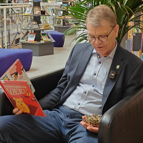 Borgmester Mikael Klitgaard sidder i lænestol på biblioteket og læser højt for pythonslange, som han holder i hånden.