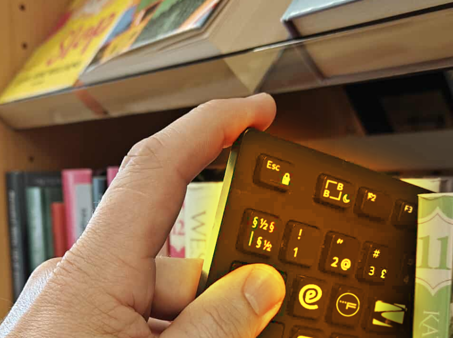 Nærbillede af hånd, der trækker et computertastatur ud mellem bøgerne på en hylde. Flere af tastaturets knapper er udskiftet med logoer for eReolen, Filmstriben etc..