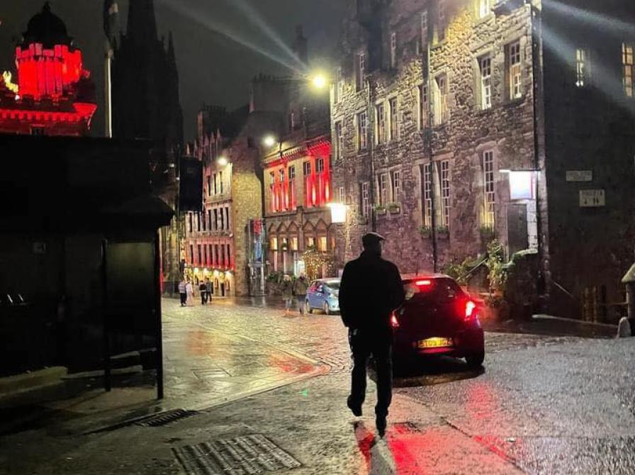 Mads Nygaard i silhouet, set fra bagfra. Omgivelserne er en aftenvåd brostensbelagt gade med gadelamper og kirketårn i Edinburgh.